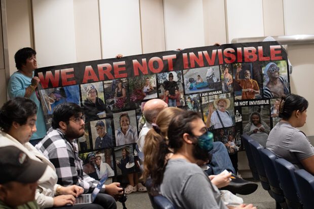 Activists hold up a banner in the Fresno City Council Chambers before a public hearing on a new homeless ordinance criminalizing the unhoused. Photo by Peter Maiden