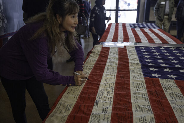Victims of the Japanese internment and their families signed their names and wrote the names of the camps where they were held on 48-star American flags. Akiko Peterson signed at a luncheon on Feb. 10 for the Day of Remembrance at the Fresno Fairgrounds. Photo by Peter Maiden