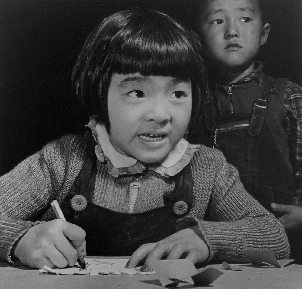 A third-grade student at the Manzanar Relocation Center for evacuees of Japanese ancestry practices free-hand drawing. This photo was taken in the student training center where student teachers were given college credit for their practice teaching. Kiyo Fukasawa is the student teacher and is supervised by a Caucasian teacher, as were all the student teachers. Photo courtesy of the Francis Stewart Gallery/NPS