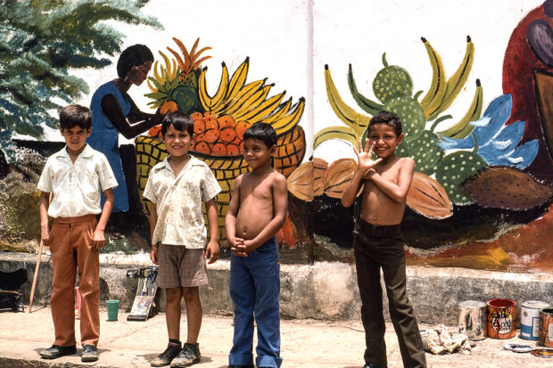 Niños posando frente a un mural en Bluefields, Nicaragua, en 1984. El gobierno nicaragüense ha aumentado el apoyo a la niñez en todo el país por medio de desayunos escolares gratis y actividades recreativas. Foto cortesía The Commons
