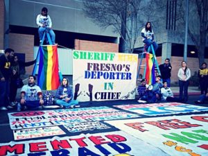 The picture shows the #not1more action that happened on December 23, 2013. After many attempts to meet with Fresno County Sheriff Mims, a group of 2 brave men and 3 women put their lives on the line to make a statement to stop all deportations and all people being detained in the Prison awaiting deportations. We also show the rainbow flags in solidarity with our queer brothers and sisters to show that they are intersecting and we will not turn our backs to our queer hemanas y hermanos. Photo by Fresno Immigrant Youth in Action (FIYA)